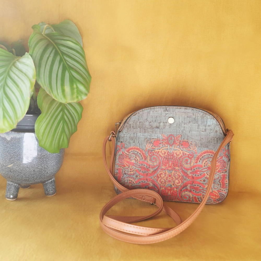 grey bleu with red floral pattern, traditional mediterranean medium crossbody handbag with light brown shoulders strap. vegan leather bag made out of cork presented on a turmeric background and a tropical plant next to it. 