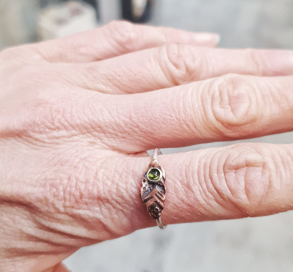 This beautiful Tribal Tourmaline Ring features a 3mm natural green tourmaline gemstone surrounded by a dainty silver band and copper leaf-shaped design.