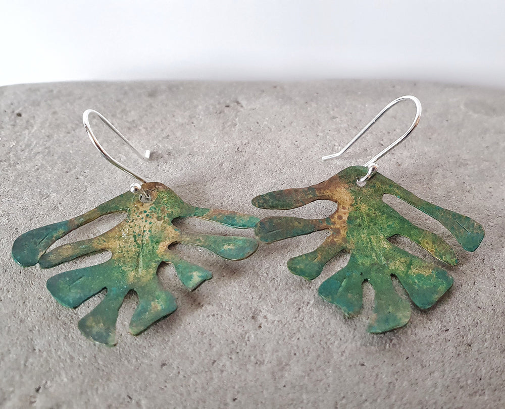 Introducing our Tropical Bliss pair, a harmonious fusion of nature-inspired elegance and artistic craftsmanship.  These exquisite earrings feature delicate tropical leaves meticulously crafted from patina brass, capturing the essence of a sunlit paradise.  Brass leaves are carefully handmade with an organic patina, hand sawn into delicate tropical leaves shapes. Hooks are in Sterling Silver.