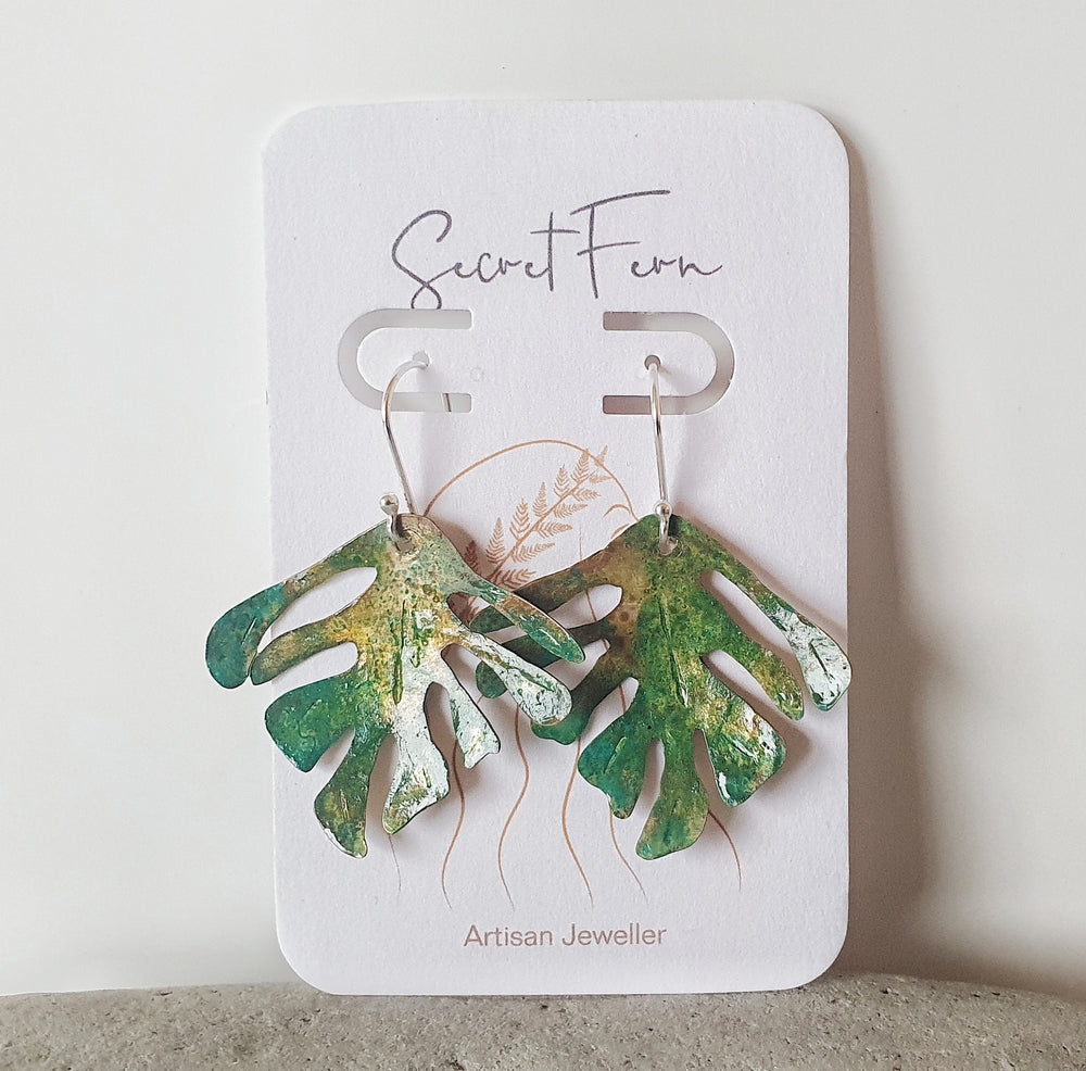 Introducing our Tropical Bliss pair, a harmonious fusion of nature-inspired elegance and artistic craftsmanship.  These exquisite earrings feature delicate tropical leaves meticulously crafted from patina brass, capturing the essence of a sunlit paradise.  Brass leaves are carefully handmade with an organic patina, hand sawn into delicate tropical leaves shapes. Hooks are in Sterling Silver.