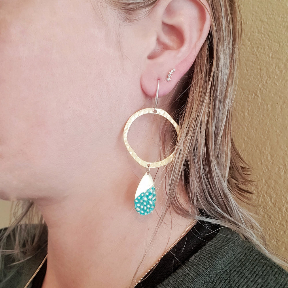 Hammered and textured brass with polished Sterling Silver posts.  Earrings are finished with an organic washed Turquoise type of patina. Earrings are worn by a model.