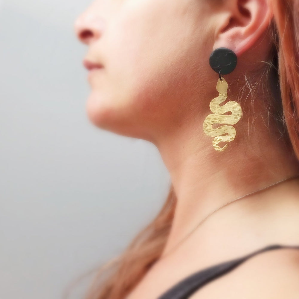 model wears a brass snake earring with a black texture stud