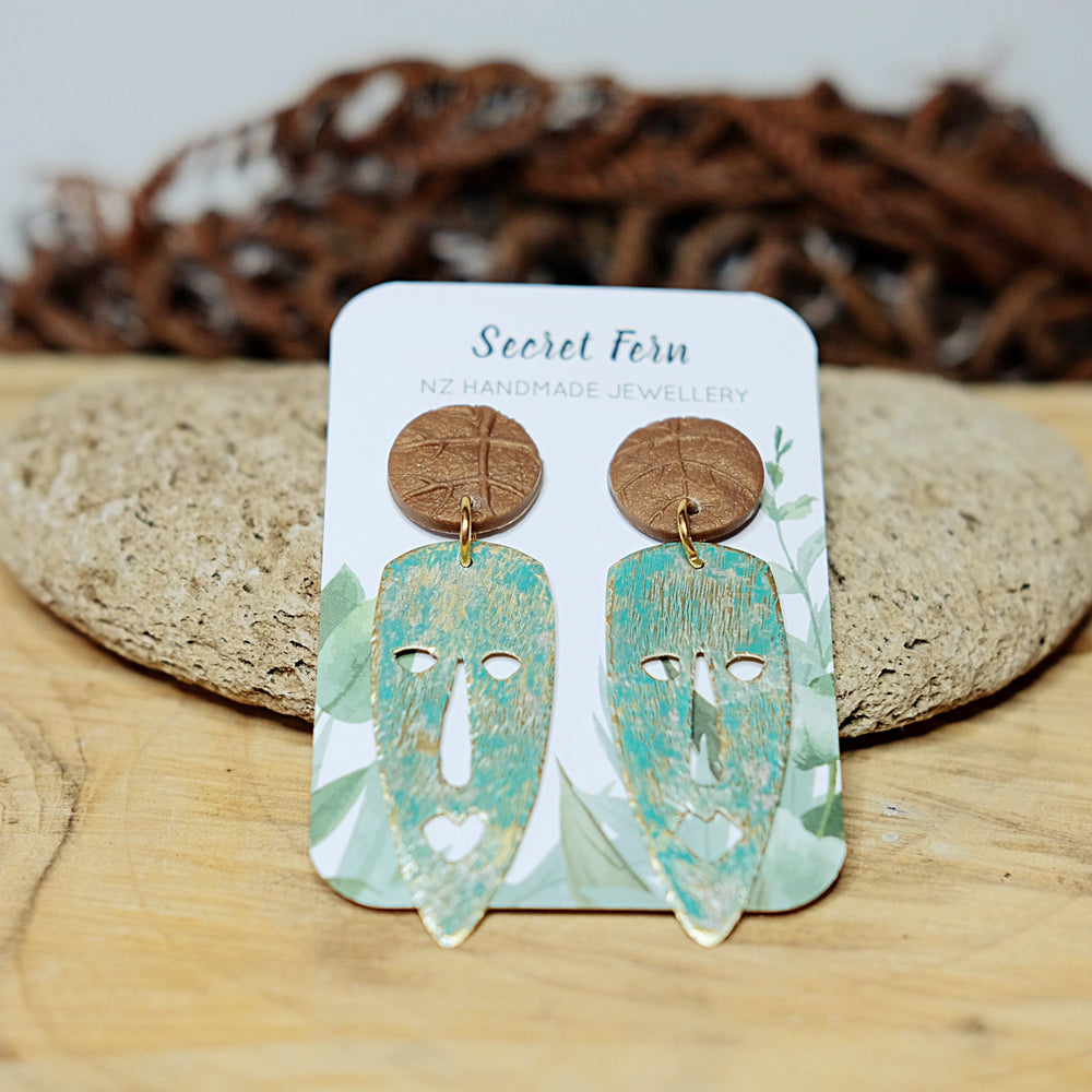 
            
                Load image into Gallery viewer, Weathered African mask brass on a foliage-stamped polymer clay stud.  Earring posts are hypoallergenic - surgical steel. 
            
        