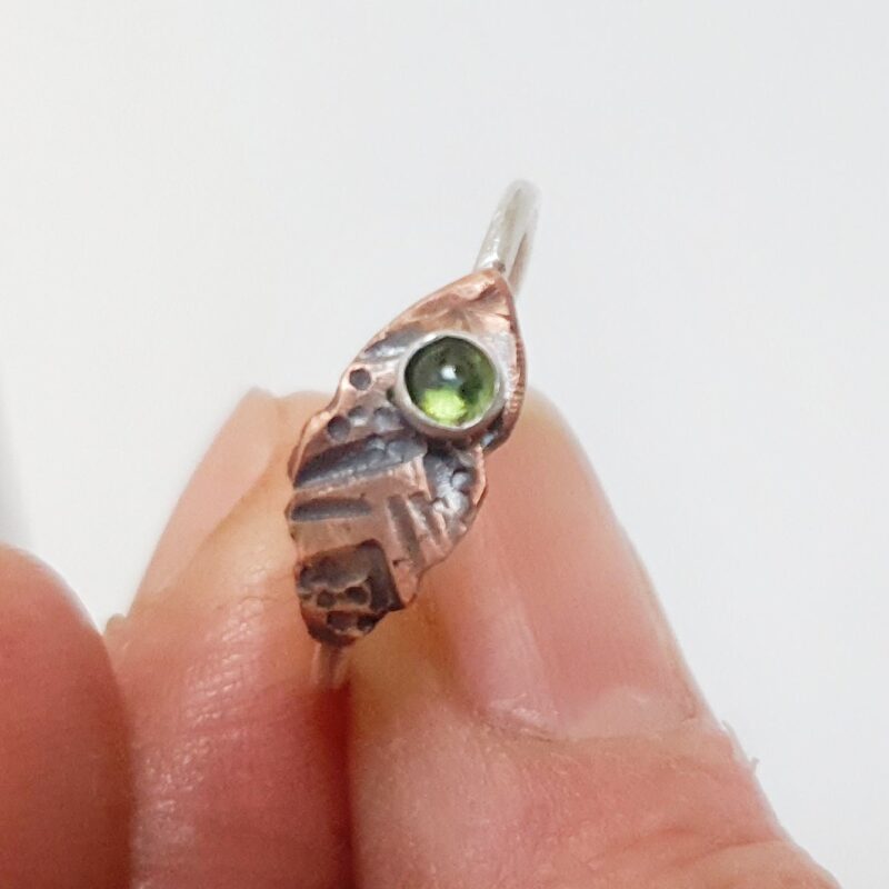 This beautiful Tribal Tourmaline Ring features a 3mm natural green tourmaline gemstone surrounded by a dainty silver band and copper leaf-shaped design.