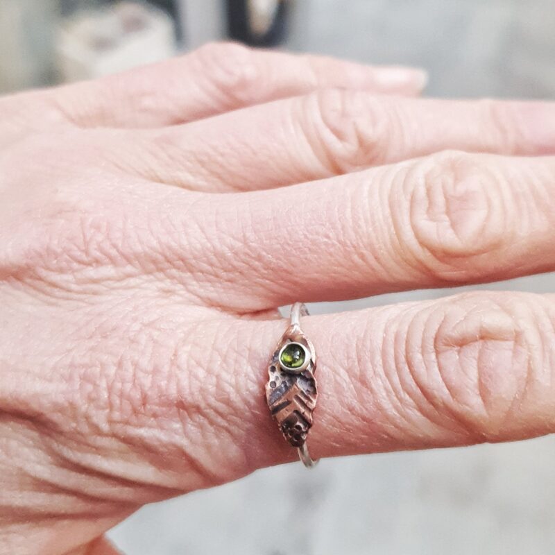 20230703_153546-01 This beautiful Tribal Tourmaline Ring features a 3mm natural green tourmaline gemstone surrounded by a dainty silver band and copper leaf-shaped design.