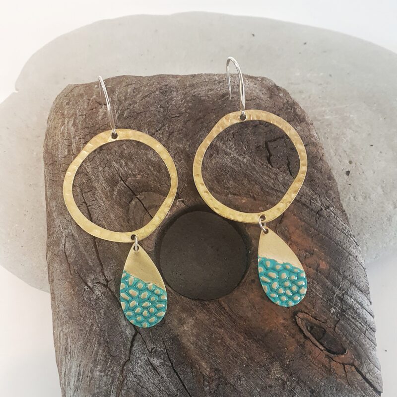 rn-image_picker_lib_temp_05d7c8e4-3d2c-48ca-9b78-4751b3684292 Hammered and textured brass with polished Sterling Silver posts. Earrings are finished with an organic washed Turquoise type of patina. Earrings are presented on a piece of drift wood.